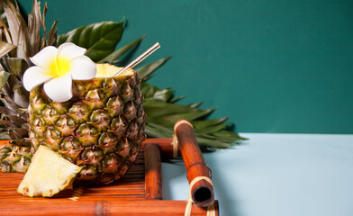 Exotic tropical cocktail drink in a pineapple with Plumeria frangipani flower and palm leaf for decoration.