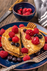 Sliced sweet homemade pancakes with raspberries and blueberries on blue plate