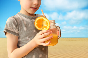 cheerful kid holds a glass jar in his outstretched hand with orange juice from an orange or lemon with a straw, the concept of a healthy diet, vitamins, lifestyle