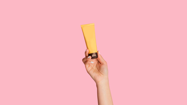 Unrecognizable Woman Showing Tube With Hand Cream Over Pink Background, Closeup