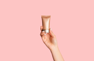 Female hand showing bottle of cosmetic foundation on pink background, closeup