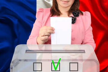 woman voter in a smart pink jacket lowers the ballot in a transparent ballot box against the background of the national flag of France, the concept of state elections, referendum