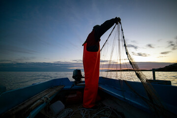 Silhouette of fisherman throwing net from boat during sunset, on Island Vis in Croatia