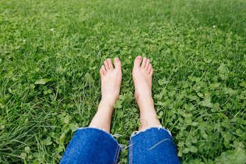 Legs woman relaxing on grass. Female feet on green grass background. Beautiful barefoot legs in the morning dew on the grass.