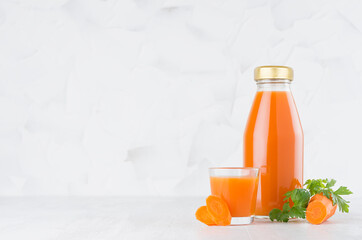 Fresh vegetable orange carrot juice in glass bottle template with glass, green parsley, slices on wood table and white background with copy space.