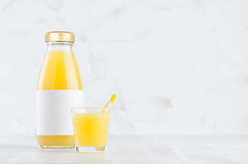 Fresh orange juice in glass bottle with blank label mock up with wine glass, straw on wood table in soft light white interior, template for packaging, advertising, design product, branding identity.