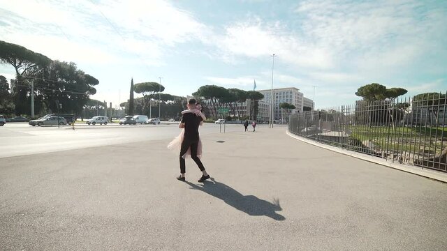 Meeting of happy couple on city background. Urban square, road traffic. The girl in the dress runs up to the guy hugs her neck, twirls and kisses. date. Summer, road and cars. Bus stop. Slow motion