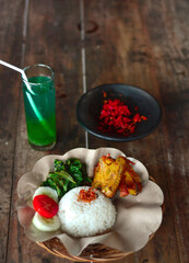 Delicious fried chicken rice with hot chili sauce, vegetables and a glass of drink on a wooden table. Indonesian special food
