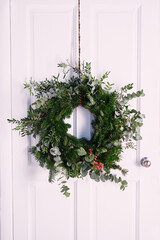 christmas wreath of fir branches and plants hanging on  white door, home decoration