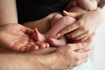 parents hold newborn baby in their arms, close-up of baby's hands and feet,