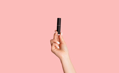 Beauty and makeup. Young lady holding tube of lipstick over pink background, closeup - obrazy, fototapety, plakaty