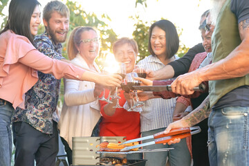 Happy family cheering and toasting with red wine in barbecue party - Chef senior man grilling meat and having fun with parents - Weekend food bbq and reunion young and older people lifestyle concept