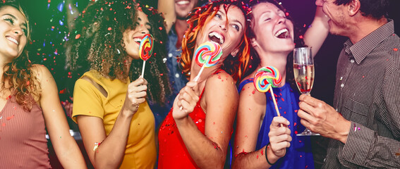 Happy friends celebrating new year eve drinking champagne in nightclub - Young people having fun dancing with lollipops in disco club - Youth culture entertainment lifestyle and nightlife concept