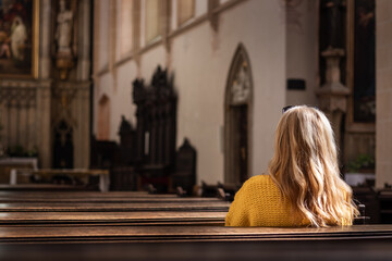 Woman sitting on pew and praying in empty church. Catholic religion at European culture