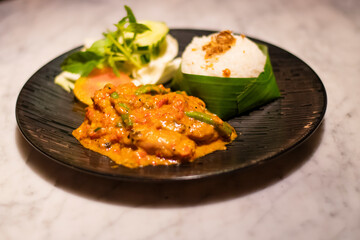 Decorated platter dinner with creamy chicken and salad served in a black plate on a wooden table in touristic visit in Bali