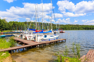 Fototapeta na wymiar Sailing boats and pier on lake shore in Karwica village port on sunny summer day, Mazury Lake District, Poland