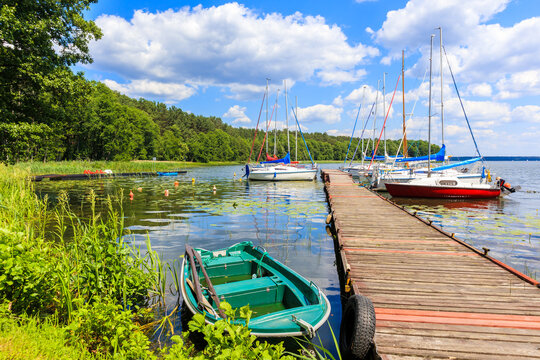 Fishing boat and yacht boats at pier on lake shore in Karwica village port on sunny summer day, Mazury Lake District, Poland