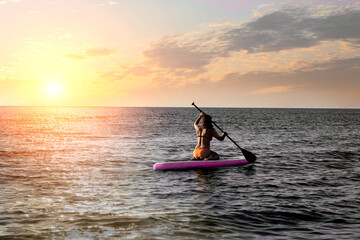 Fototapeta na wymiar Girl on paddle board sup, sea with warm sunset colors. Relaxing on ocean