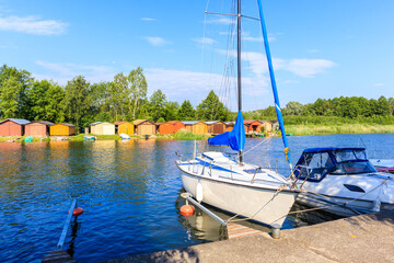 Boats anchoring in Pisz sailing port on Lake Ros on summer sunny day with fisherman houses in background, Masurian Lakes, Poland