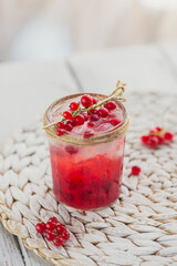 Glass of red currant cocktail or mocktail, refreshing summer drink with crushed ice and sparkling water on a white wooden background.