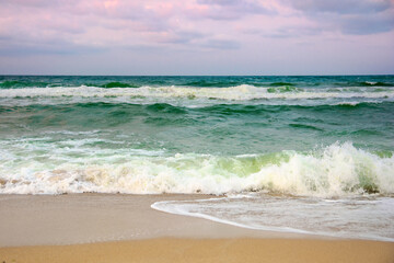 Fototapeta na wymiar dramatic weather on the seashore. green waves crashing on the beach. cloudy purple sky in evening light