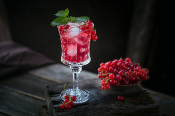Glass of red currant cocktail or mocktail, refreshing summer drink with crushed ice and sparkling water on a dark wooden background