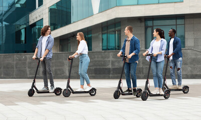 Obraz premium Five friends having pleasant ride on motorized kick scooters