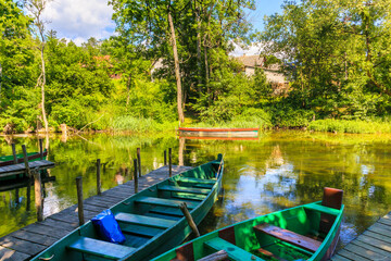 Wooden boats at pier on bank of Krutynia river where tourists do kayaking during summer months, Masurian Lakes, Poland