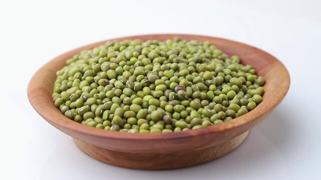 Rotating of mung beans in wooden plate on white background. Side view, close up.