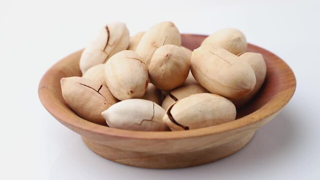 Rotating of raw pecan nuts in wooden plate on white background. Side view, close up.