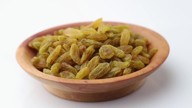Rotating of raisins in wooden plate on white background. Side view, close up.