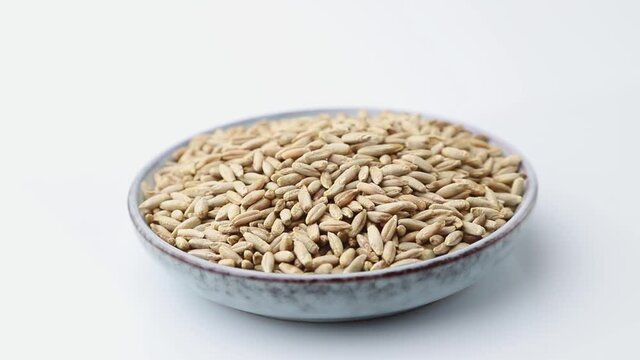 Rotating of rye grains in ceramic plate on white background. Side view, close up.