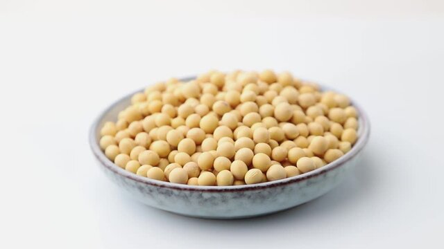 Rotating of soy seeds in ceramic plate on white background. Side view, close up.