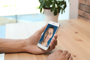 Man using smartphone with facial recognition system at table indoors, closeup. Biometric...
