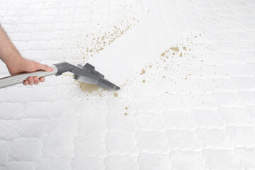 Man disinfecting mattress with vacuum cleaner, closeup
