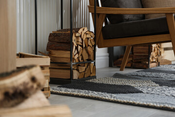 Firewood near armchair in stylish room interior