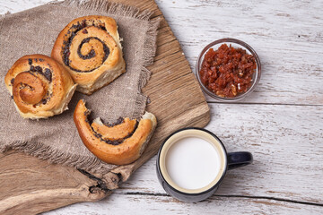 Variety of homemade puff pastry buns cinnamon served with milk cup, jam, butter as breakfast over white plank wooden background. Flat lay, space