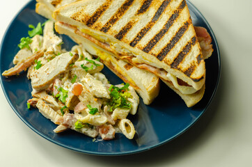 White bread with beechwood smoked bacon, egg, mayonnaise, and tomato served with Caesar pasta with parmesan cheese on the blue plate