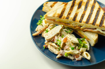 White bread with beechwood smoked bacon, egg, mayonnaise, and tomato served with Caesar pasta with parmesan cheese on the blue plate