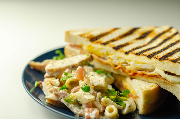 White bread with beechwood smoked bacon, egg, mayonnaise, and tomato served with Caesar pasta with parmesan cheese on the blue plate