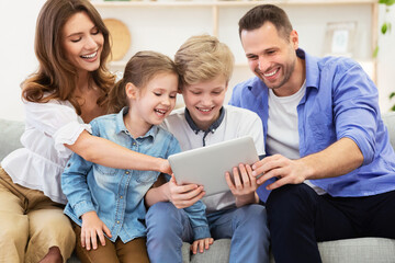 Parents And Kids Using Tablet Sitting On Sofa At Home