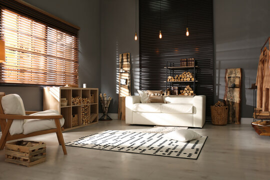 Shelving unit with stacked firewood and comfortable sofa in stylish room interior