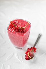 Healthy appetizing wild berry smoothie topped with redcurrant berries served in a glass with a spoon on a side, white background. Clean eating, detox concept.