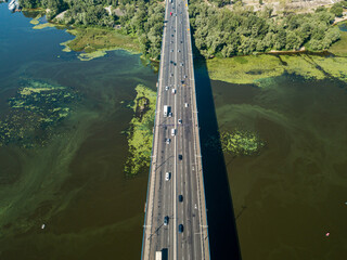 Cars travel along the North Bridge in Kiev. Green blooming algae in the Dnieper river on a hot...