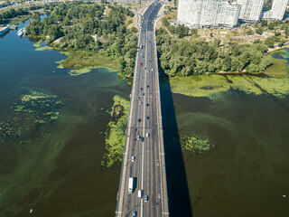 Cars travel along the North Bridge in Kiev. Green blooming algae in the Dnieper river on a hot...