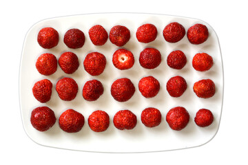 Strawberries lie in a row on a plate on a white background. The view from the top. Red berries close-up.