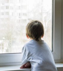 A little boy looks out the window. The street is bright and sunny. Cold weather