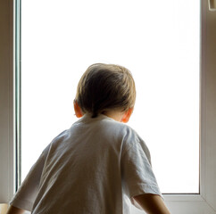 A little boy looks out the window. The street is bright and sunny. Cold weather