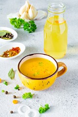 Homemade chicken (bone) broth/bouillon with vegetables, spices and herbs in a bowl (cup) on a light background. Natural collagen of animal origin. Liquid broth from meat, fish, vegetables.