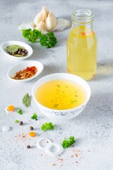 Homemade chicken (bone) broth/bouillon with vegetables, spices and herbs in a bowl (cup) on a light background. Natural collagen of animal origin. Liquid broth from meat, fish, vegetables.